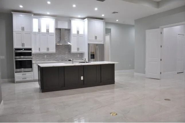 Modern kitchen with white cabinets, dark island, stainless steel appliances, and gray walls.