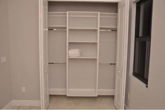 Empty white closet with shelves and rods; doors are open.