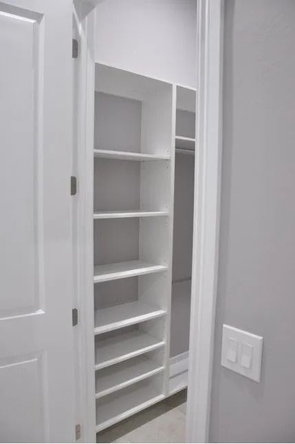 White closet with shelves, door open; gray walls, light switch visible.