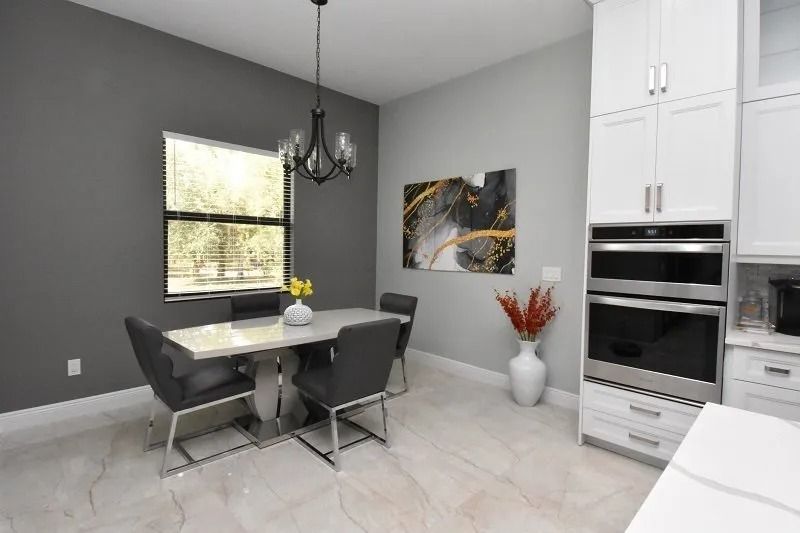 Dining area with a table, chairs, art, window, and white kitchen cabinets.