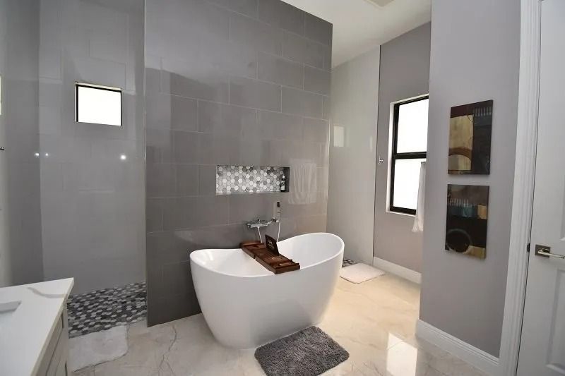 Modern bathroom with a white tub, gray tiled walls, and marble floor.