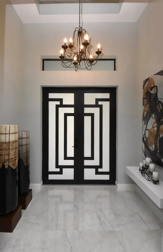 Entryway with modern black door, chandelier, white marble floor, and gray walls.