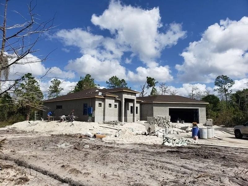 House under construction with gray walls and roof against a cloudy blue sky.