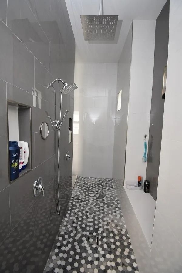 Modern shower with gray and white tiles, pebble floor, showerheads, and recessed shelves.