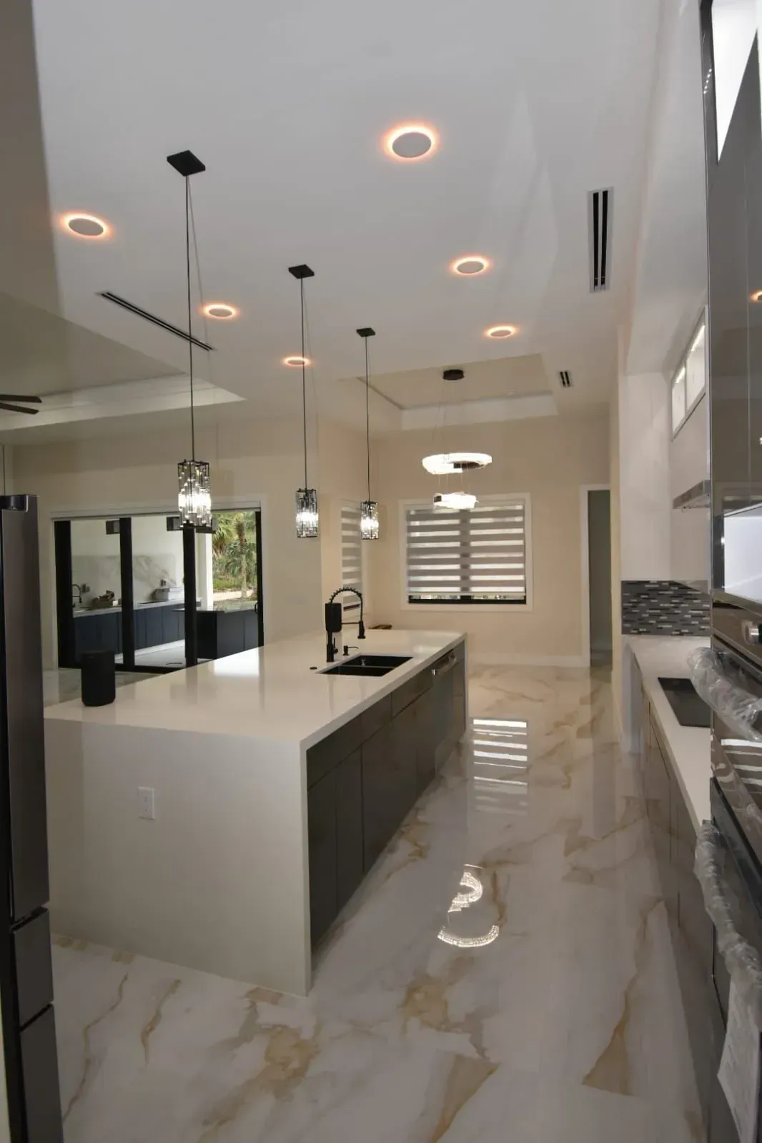 Modern kitchen with white countertops, dark cabinetry, pendant lights, and marble floors.