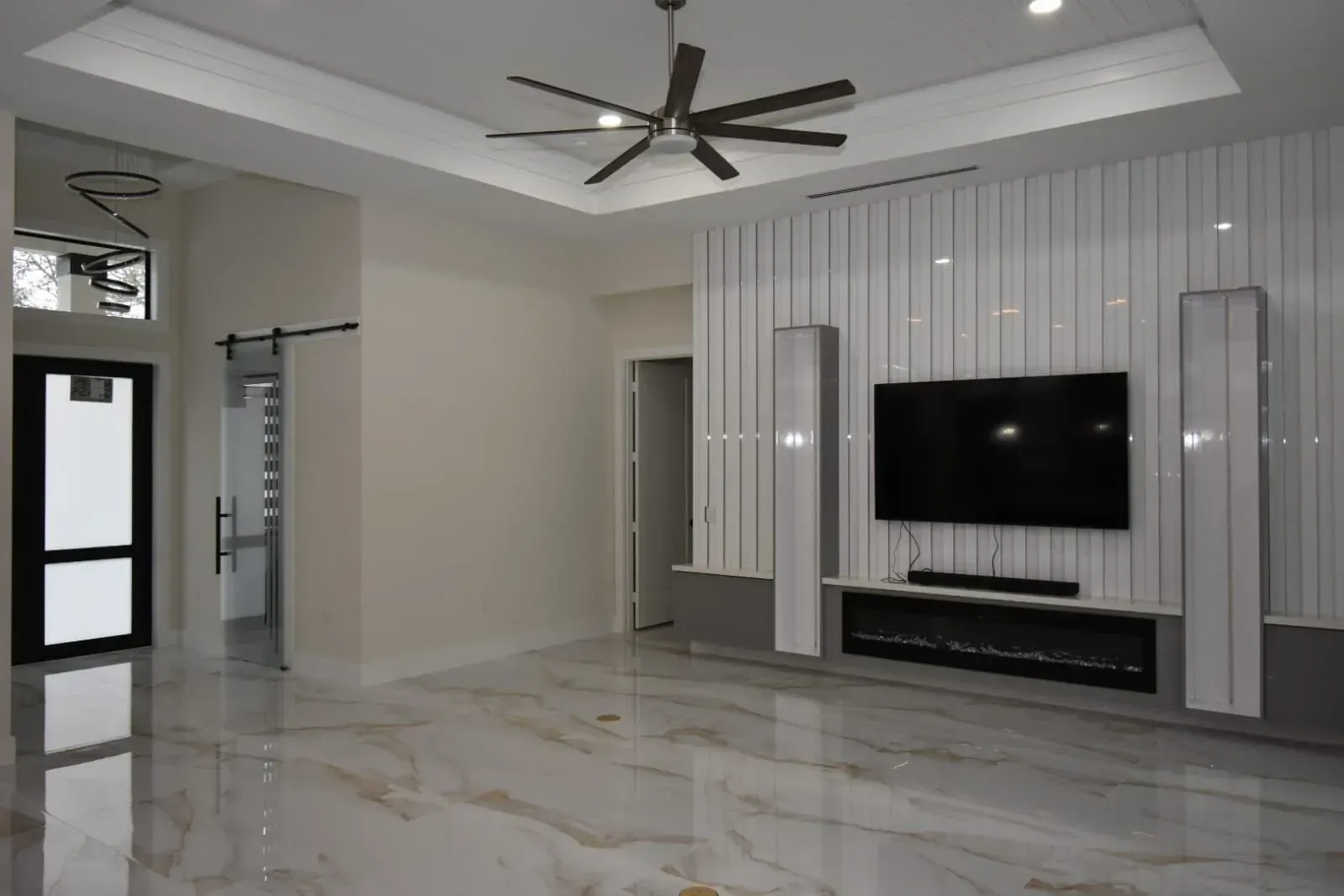 Spacious living room with marble floors, a fireplace, and a large-screen TV mounted on a white vertical-slat wall.