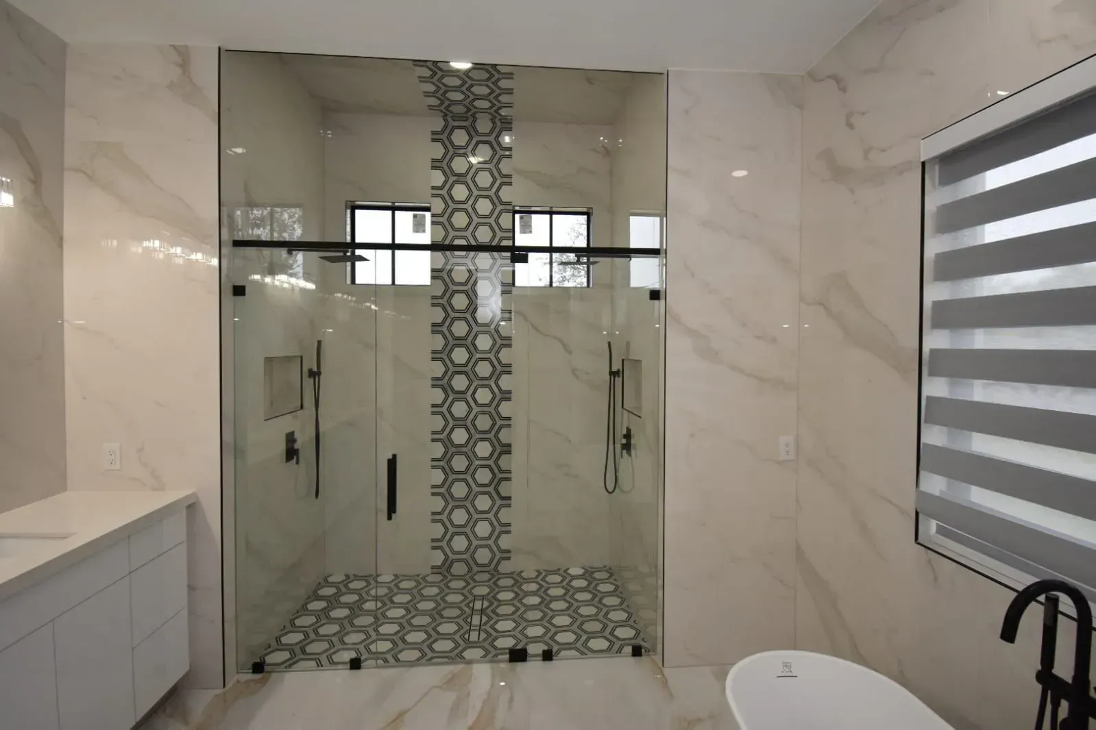 Bathroom with glass shower, white walls, black fixtures, and patterned tile.