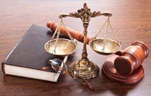 A judge's gavel, scales of justice, and a book on a wooden table.