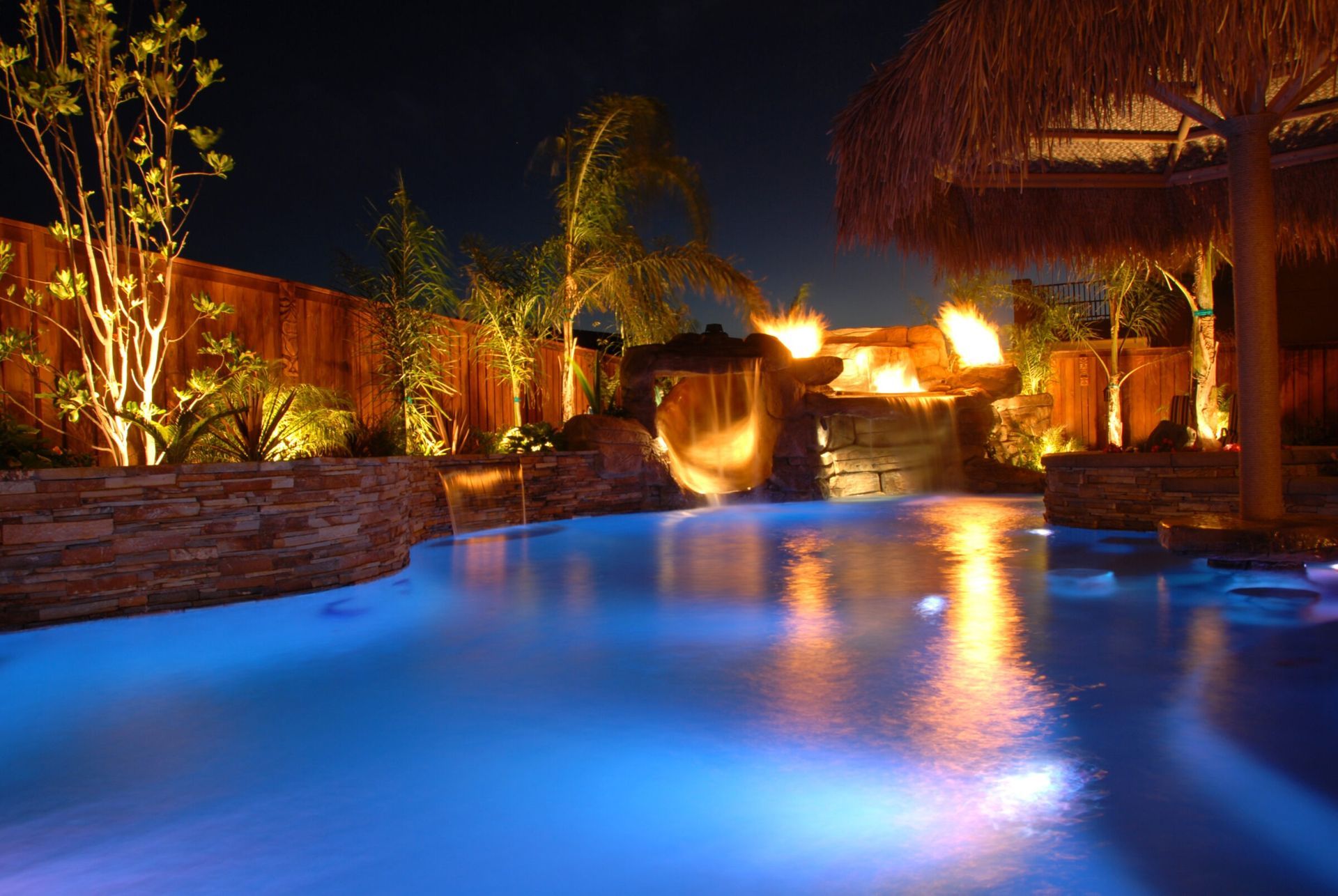 An inground pool at night with outdoor lighting.
