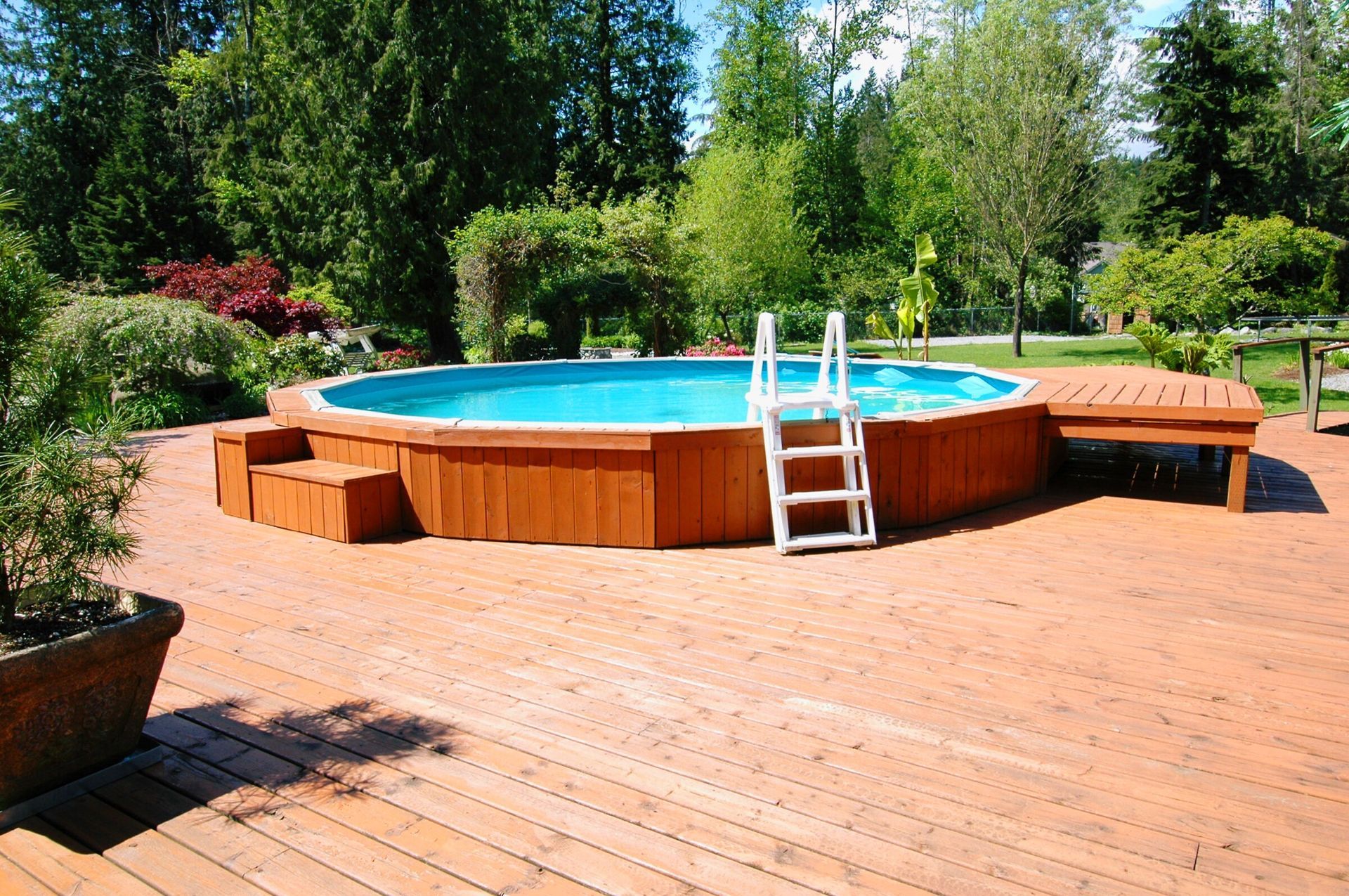An above-ground pool surrounded by a wood deck and landscaping.