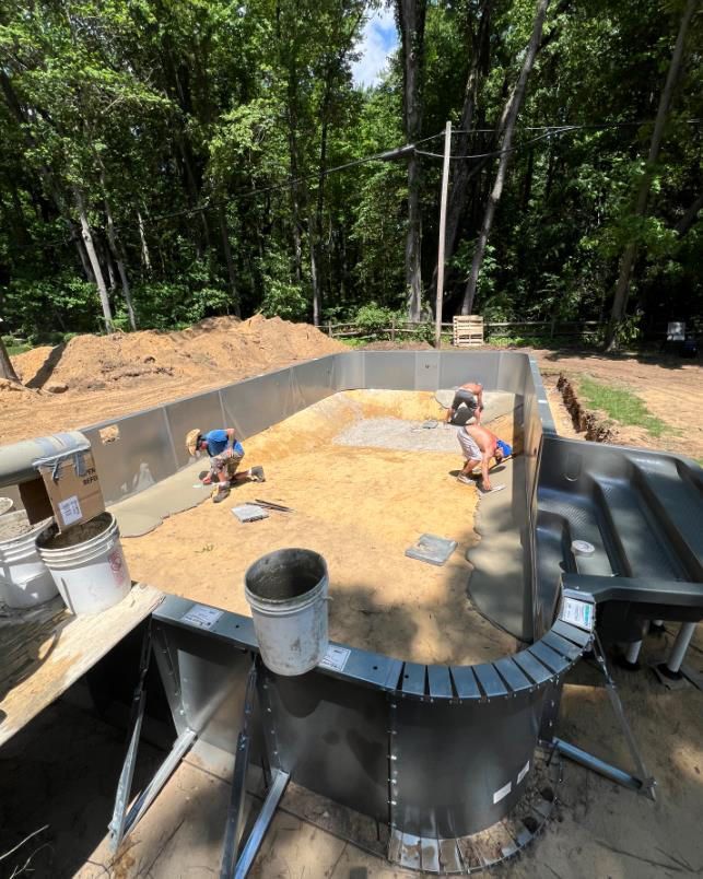 Workers installing tiles in a partially built in-ground swimming pool. Forest in background.