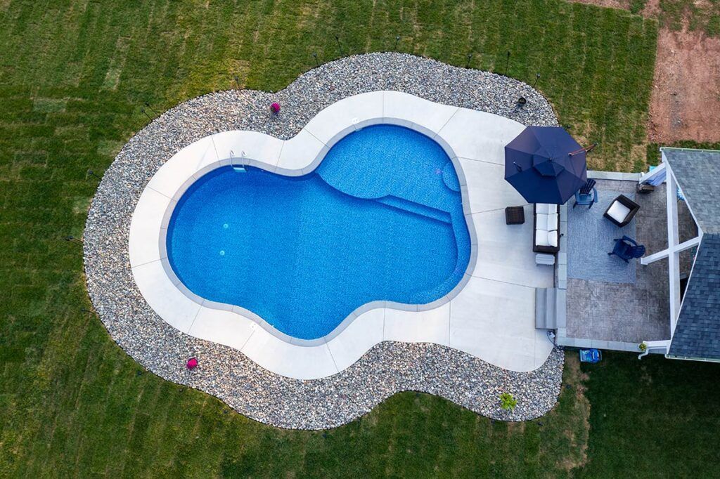Aerial view of a guitar-shaped pool surrounded by rocks and grass, with a patio and house visible.