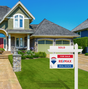 A two-story suburban home with green trim and a stone exterior, featuring a RE/MAX 