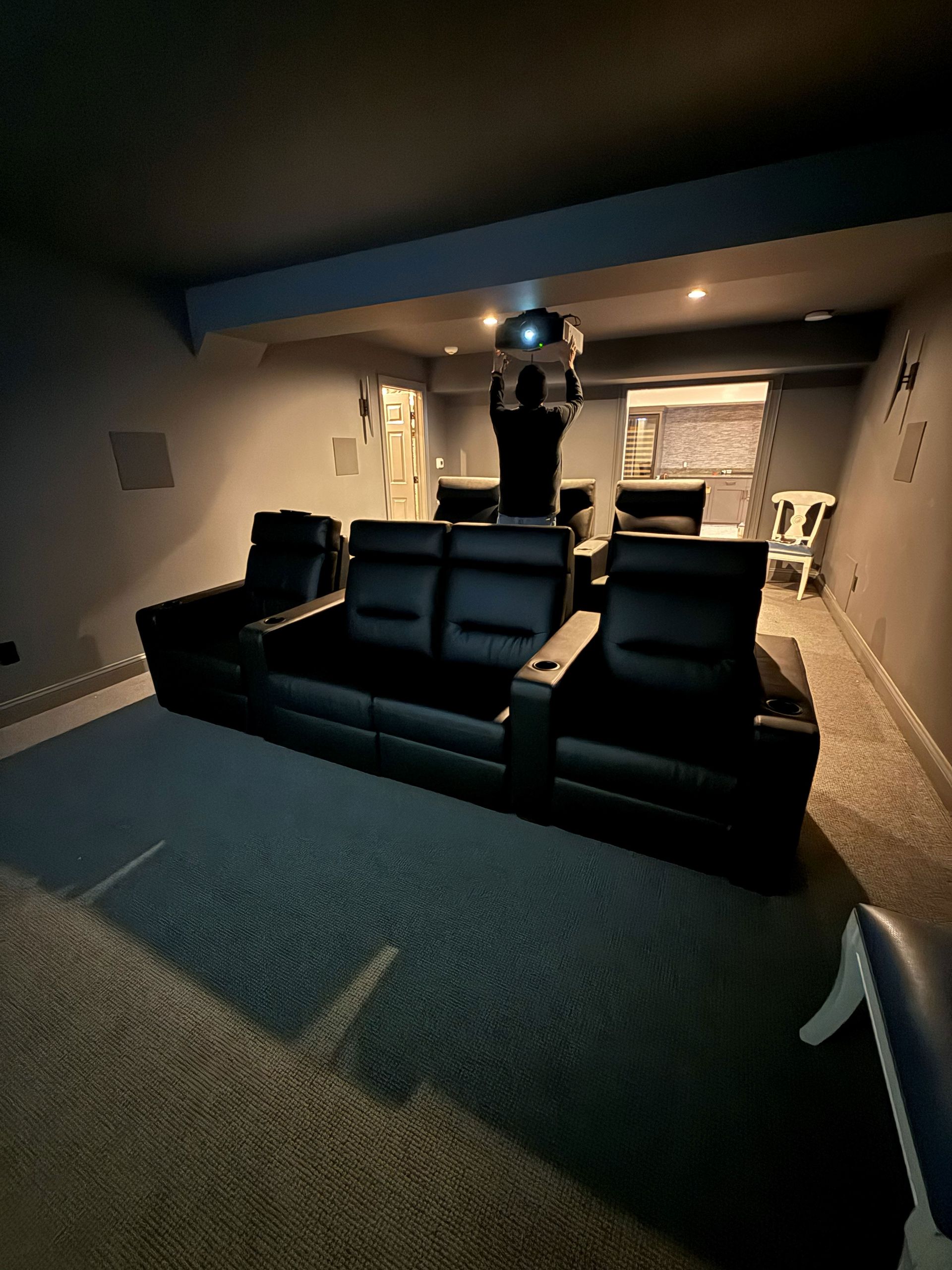 Home theater with black leather seating, a projector, and gray walls.