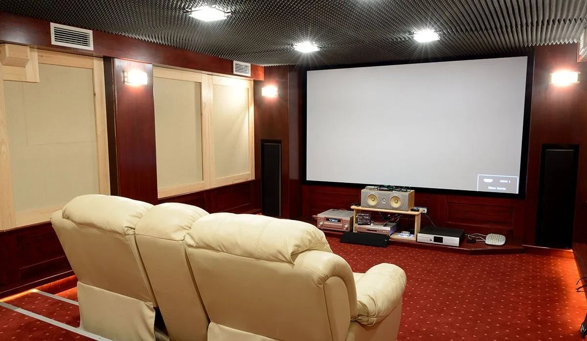 Home theater room with a large screen, two beige recliners, and red carpet.