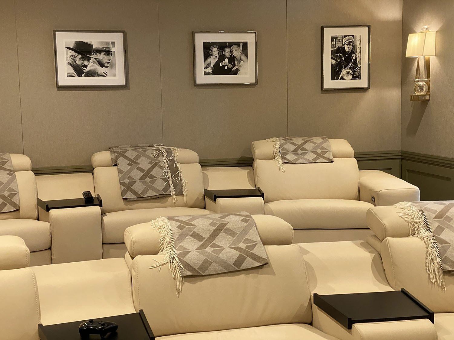 Home theater with cream-colored reclining seats, black tables, gray blankets, and framed black and white photos on the wall.