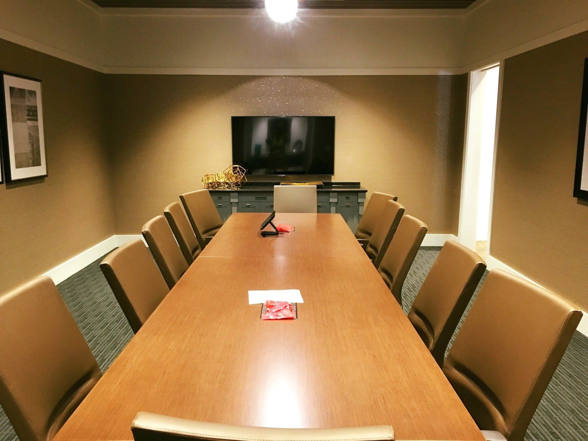 Conference room with long wooden table, chairs, TV, and artwork on walls.