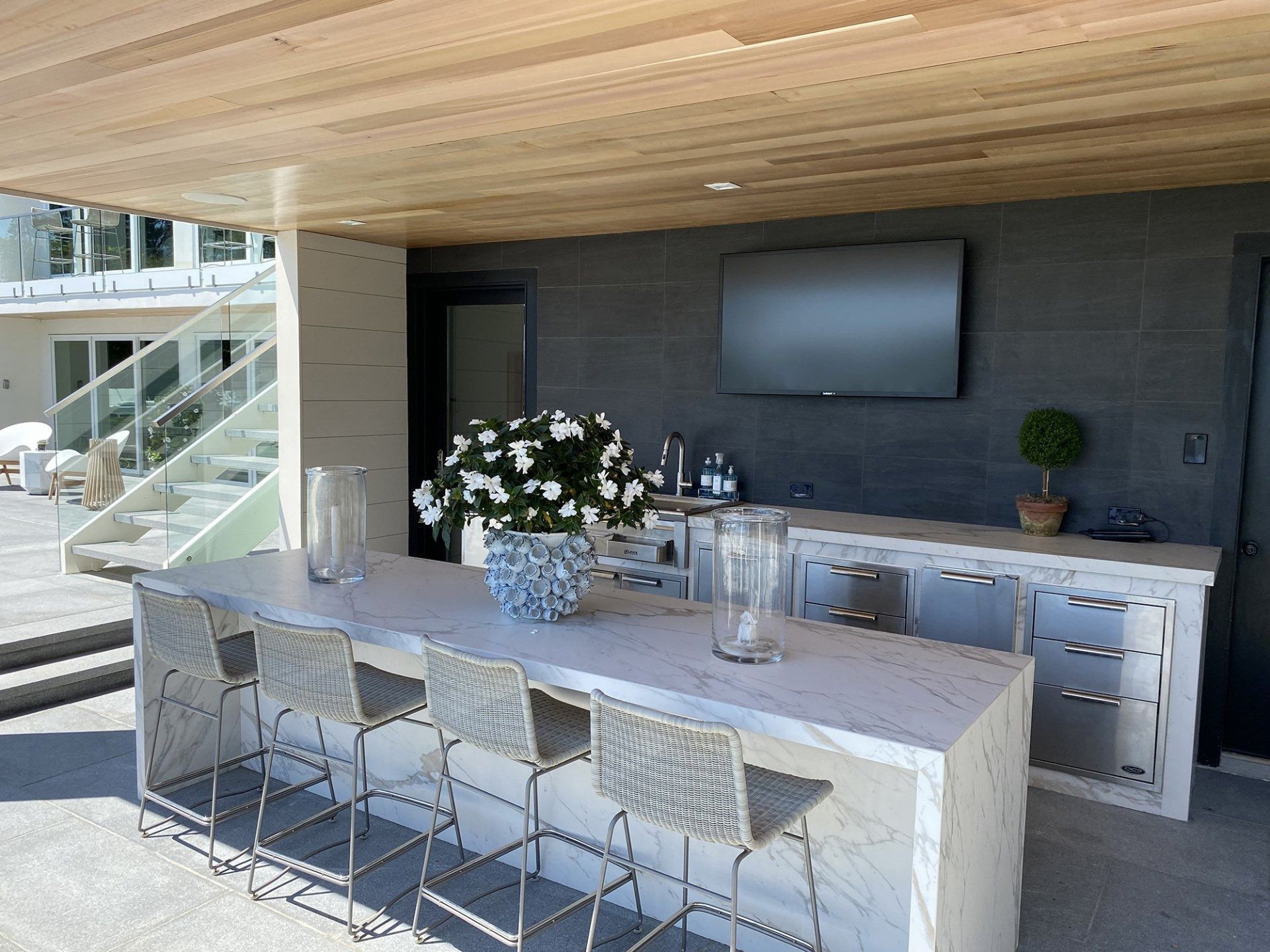 Outdoor bar with a marble countertop, bar stools, TV, and flower arrangement.