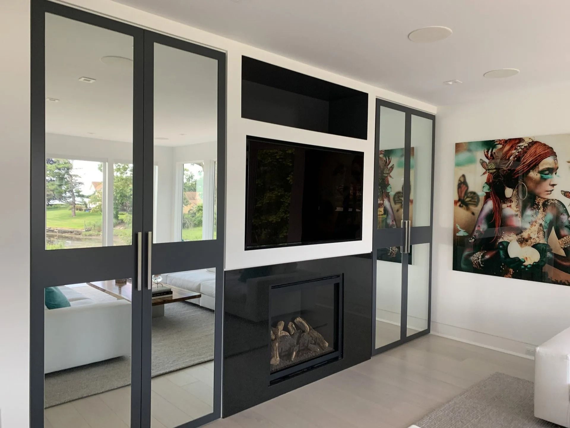Modern entertainment center with fireplace, built-in TV, flanked by mirrored doors, white walls.