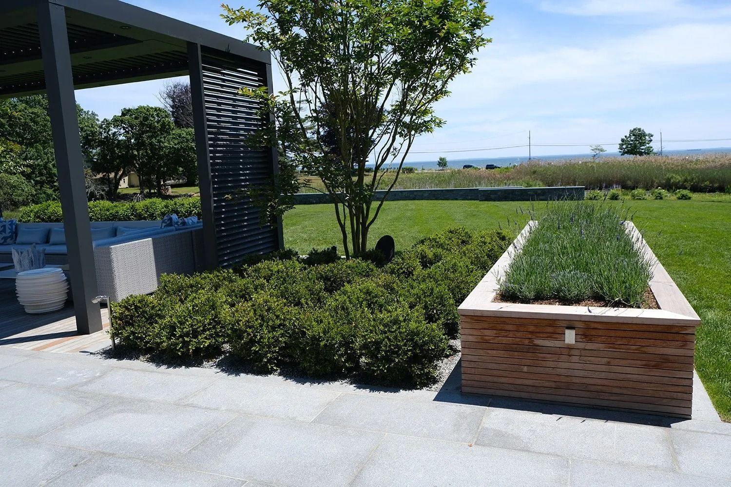 Outdoor landscaping with green plants, a wooden planter, and a pergola.