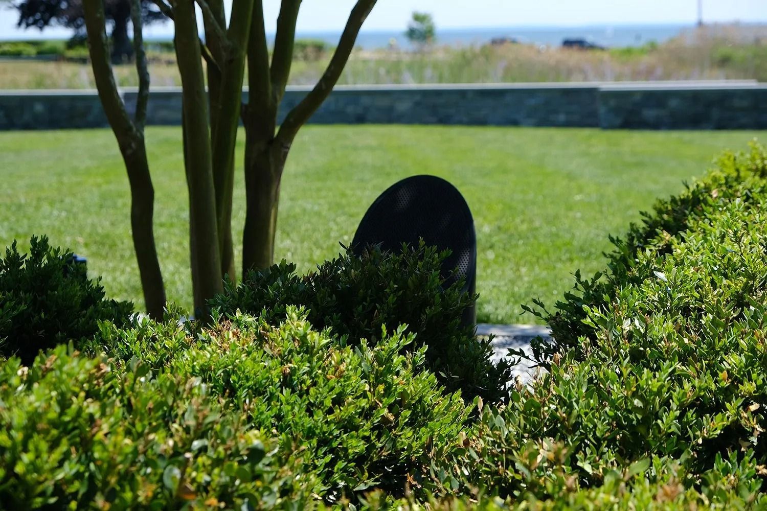 Black tombstone behind green bushes, with green lawn and sea in the background.