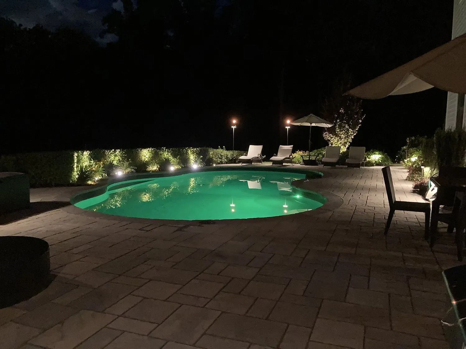 Nighttime shot of a lit pool surrounded by patio furniture and trees.