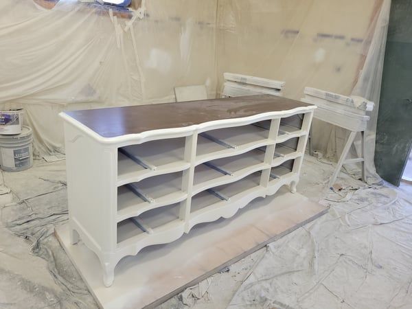 A white dresser with a brown top is being painted in a room