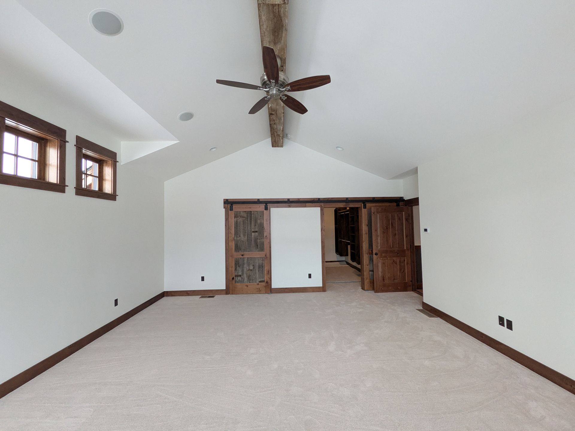 Empty bedroom with white walls, carpet, wooden trim, and a vaulted ceiling.