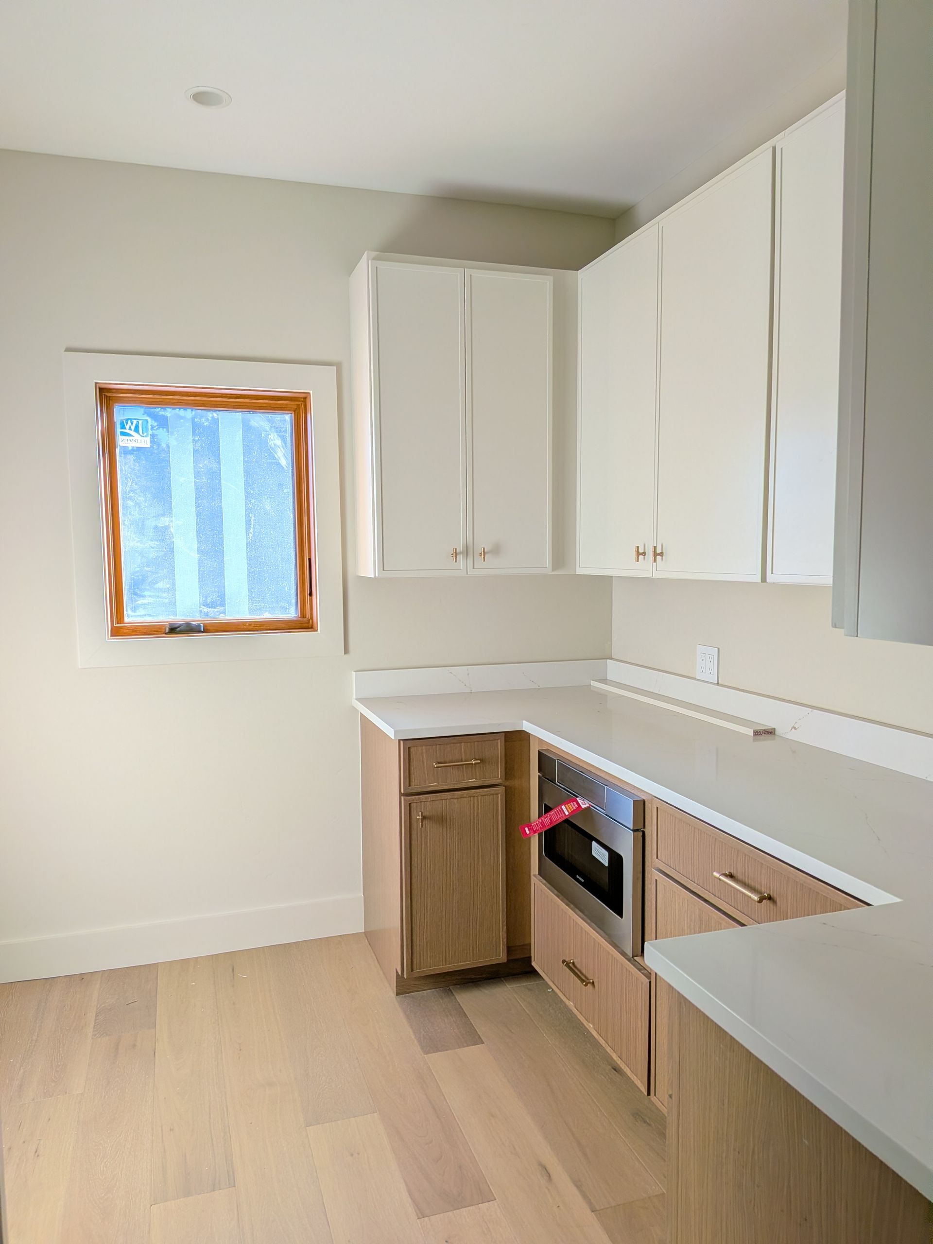 A modern kitchen with light wood and white cabinetry, a window, and light countertops.