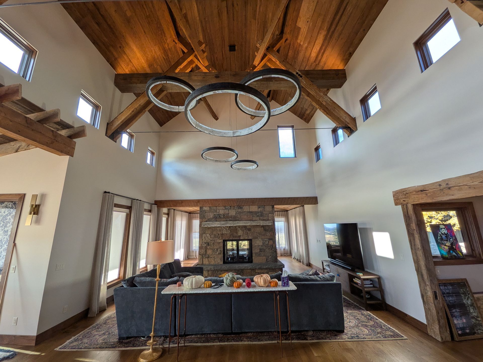 Living room with vaulted ceiling, exposed wooden beams, stone fireplace, and modern chandelier.
