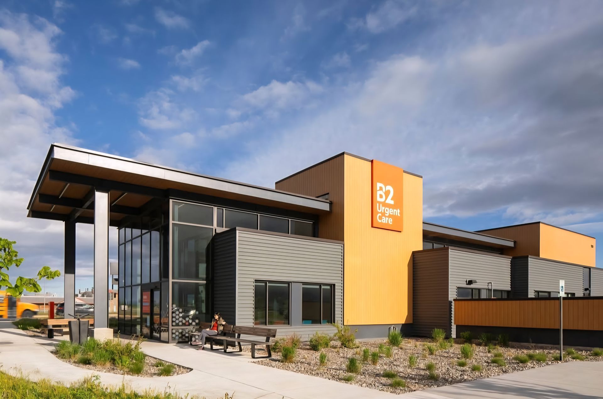 Modern building with orange and gray facade, large windows, and a covered entrance. The building has a sign that says
