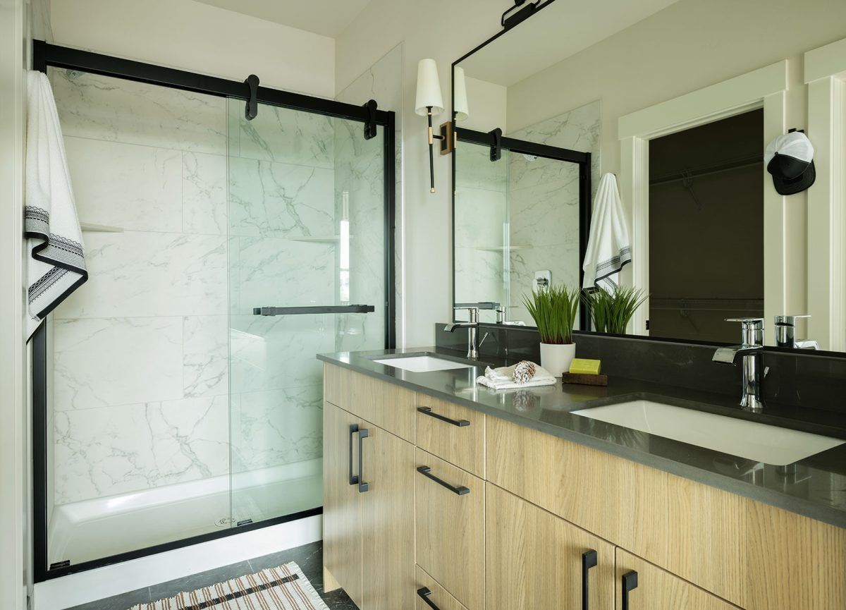 Modern bathroom with a wood vanity, double sinks, black framed mirror, and a glass shower enclosure.