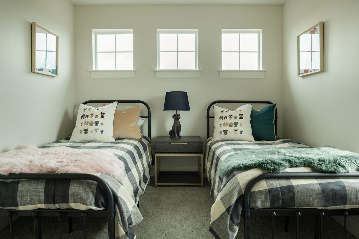 Two twin beds in a bedroom with neutral walls. Each bed has a checked blanket and pillows. A nightstand with a lamp sits between the beds.