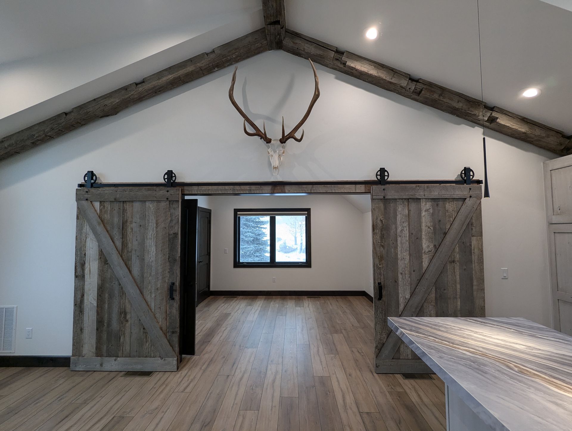Rustic interior with barn doors, antler mount, and exposed beams. The space has light wood floors and white walls.