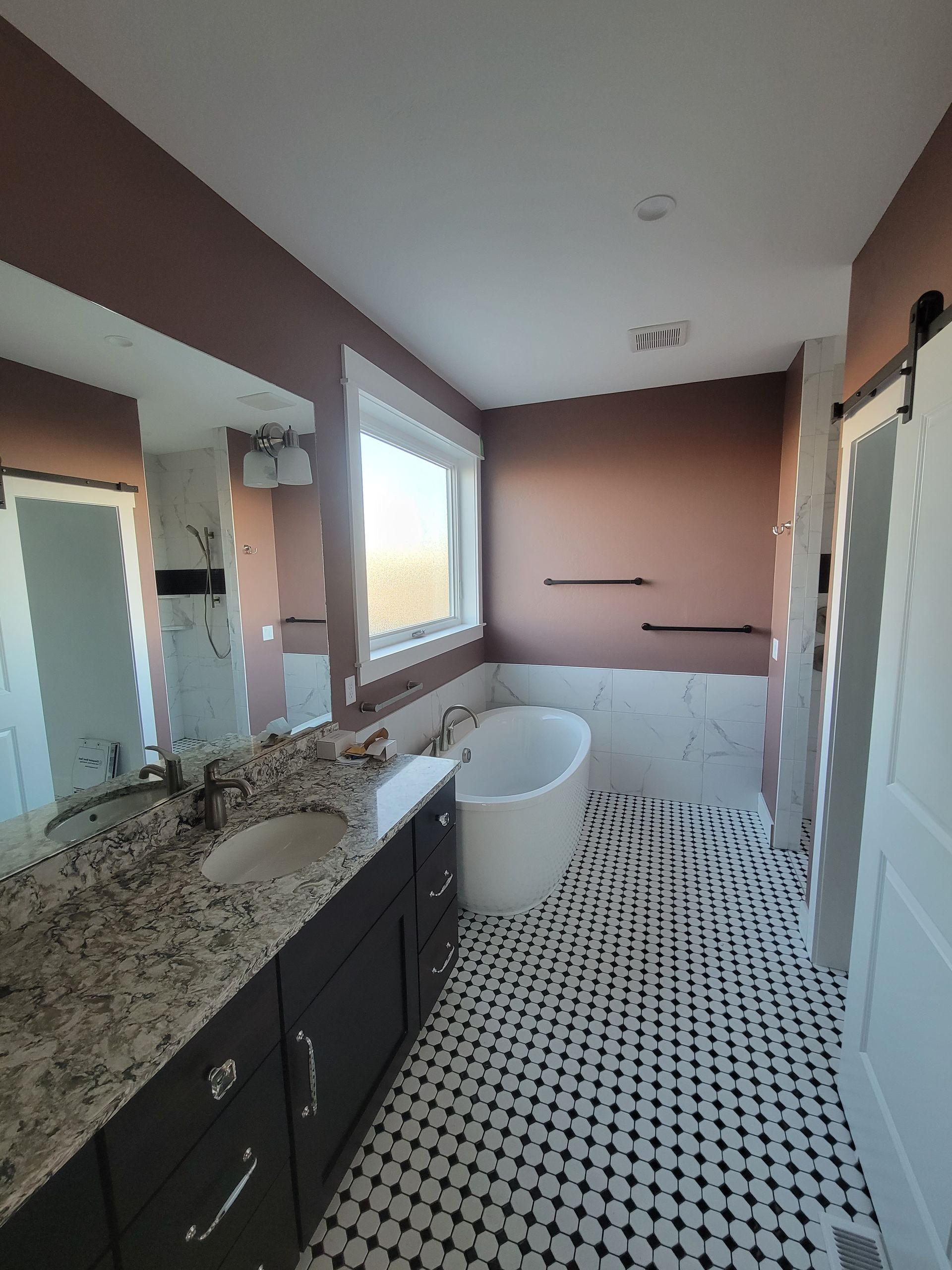 A newly renovated bathroom with a dark brown vanity, white bathtub, and black and white tile flooring. The walls are painted a muted rose color.