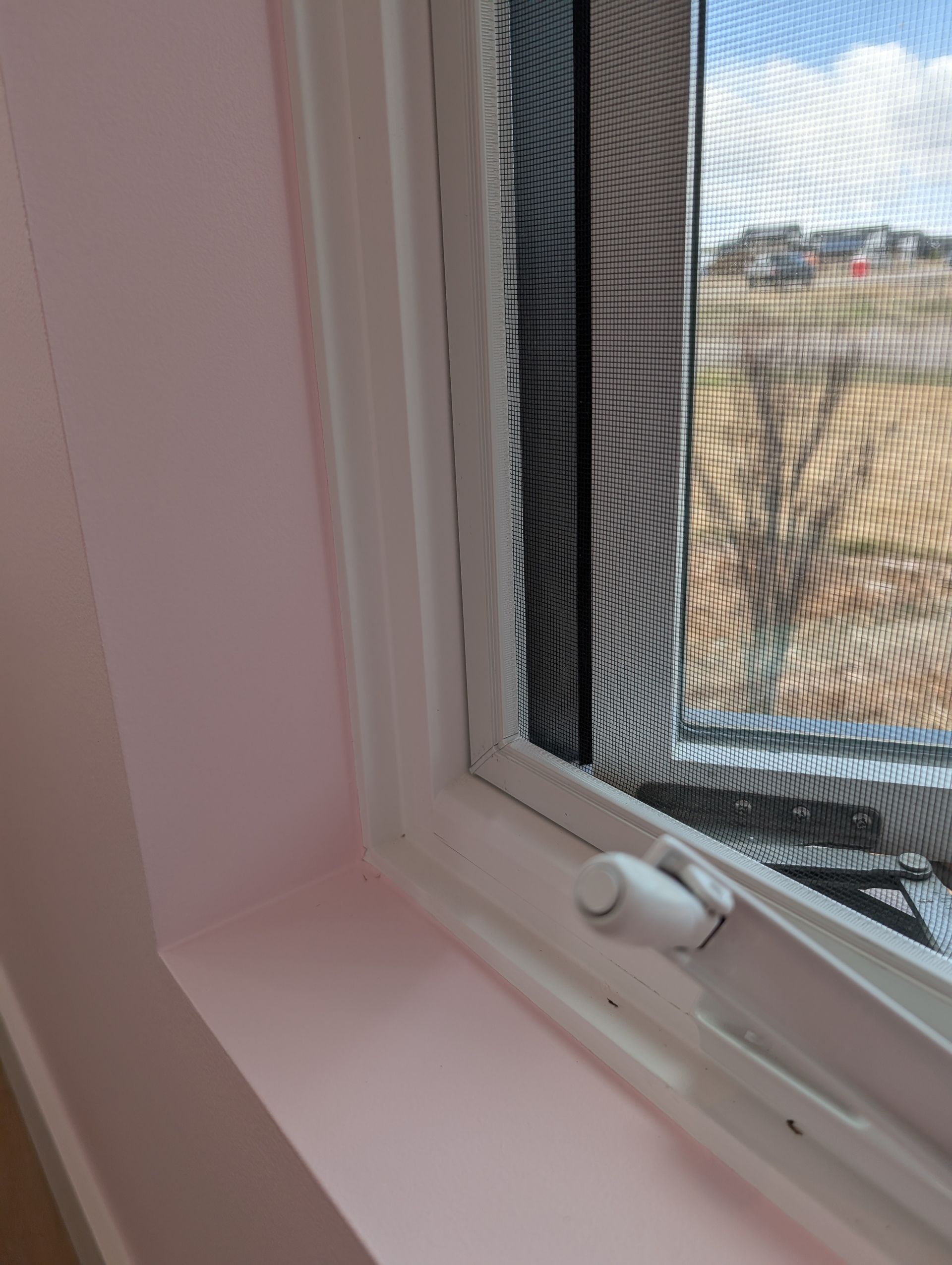 Close-up of a white-framed window with a screen and a pink wall. A white latch is visible.
