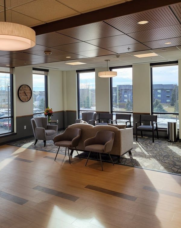 A living room with a couch , chairs , and a clock on the wall.