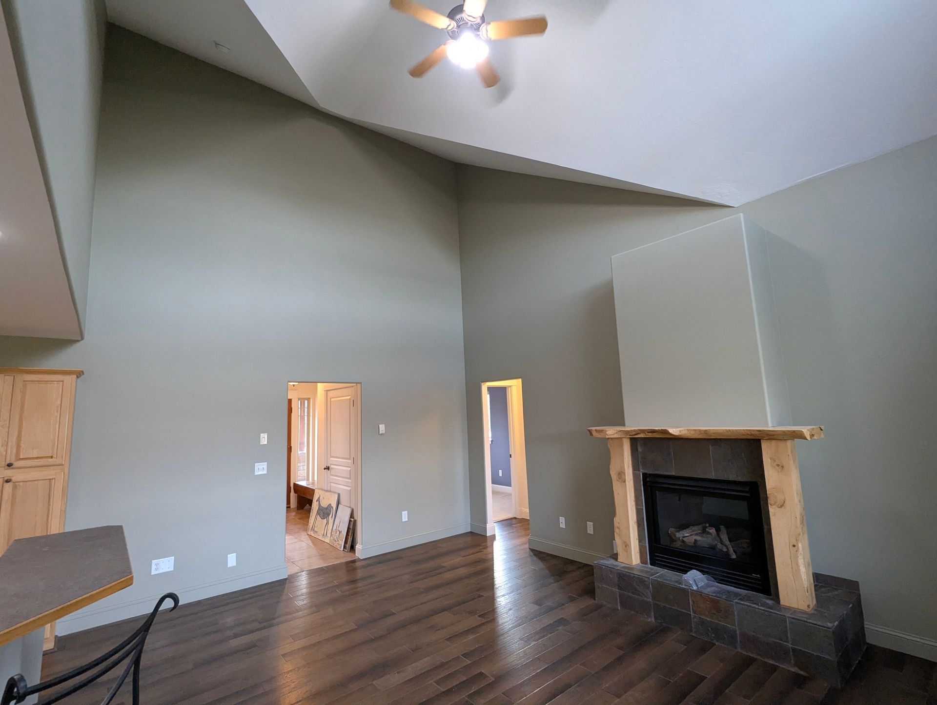 Spacious living room with vaulted ceiling and fireplace, painted green. Dark wood flooring and natural wood trim.