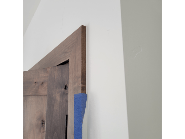 A wooden door is being installed on a white wall.