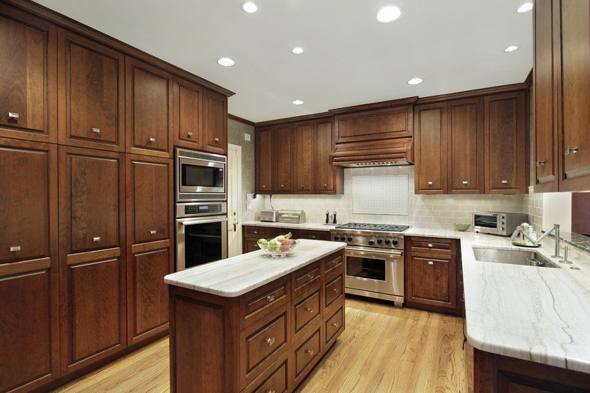 Dark wood kitchen with island, stainless steel appliances, and light-colored countertops.