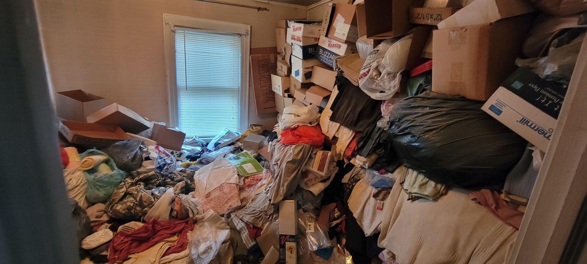 Pile of flood-damaged furniture and trash bags in front of houses, indicating cleanup efforts.