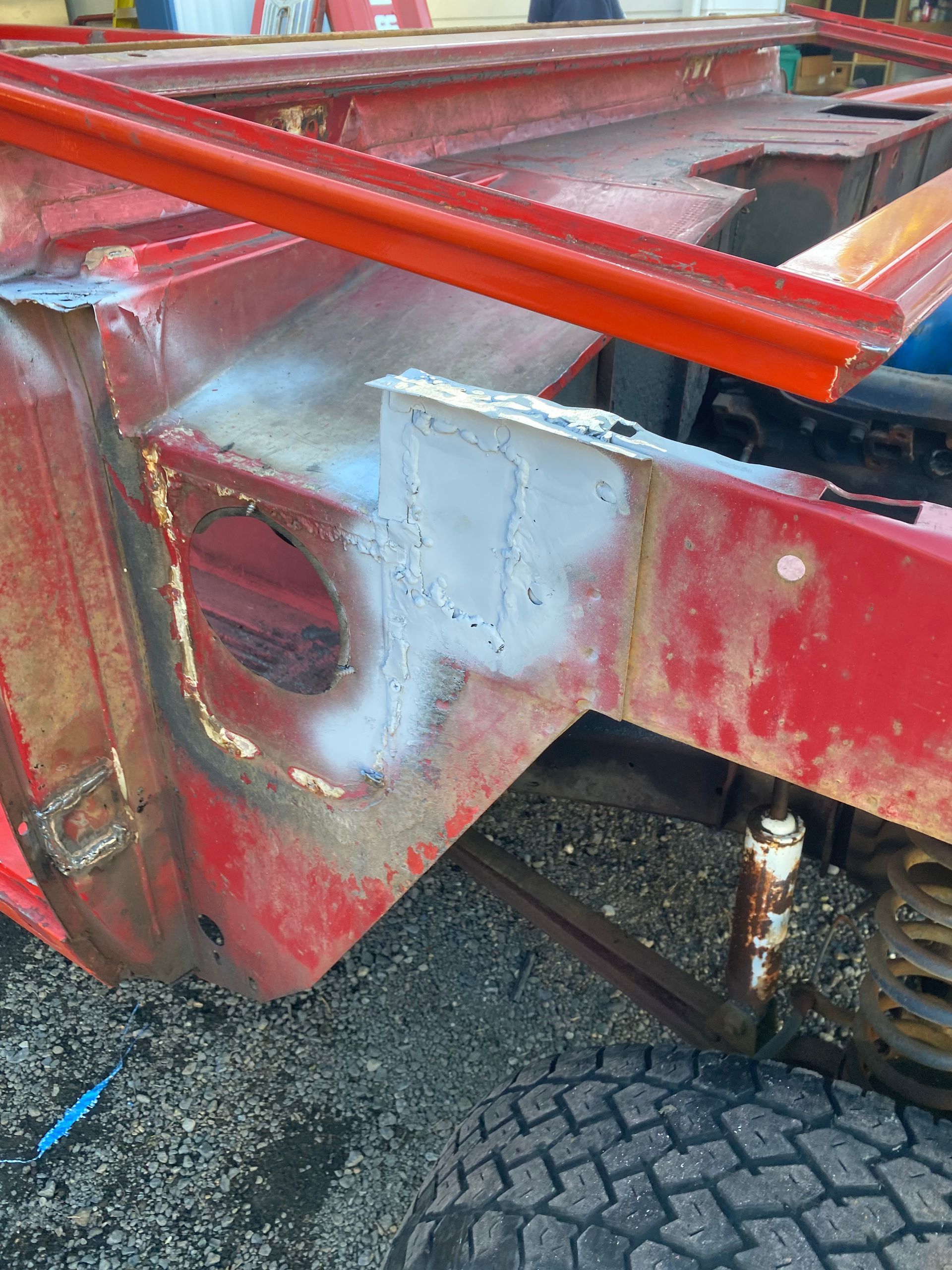 Red vehicle chassis with rusted metal, a round hole, and a silver repair patch.