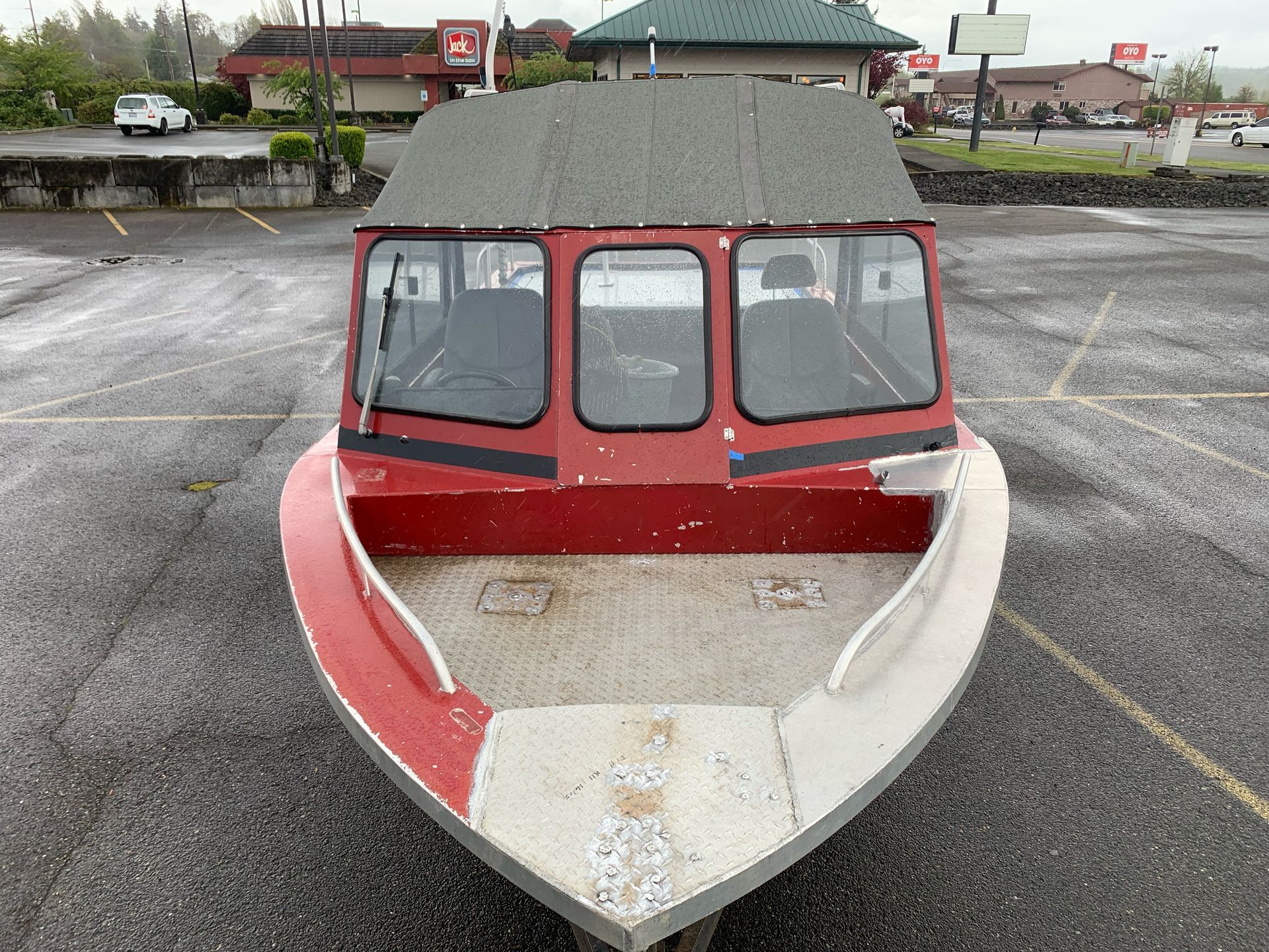 Red and silver boat parked on pavement in front of a shopping area.