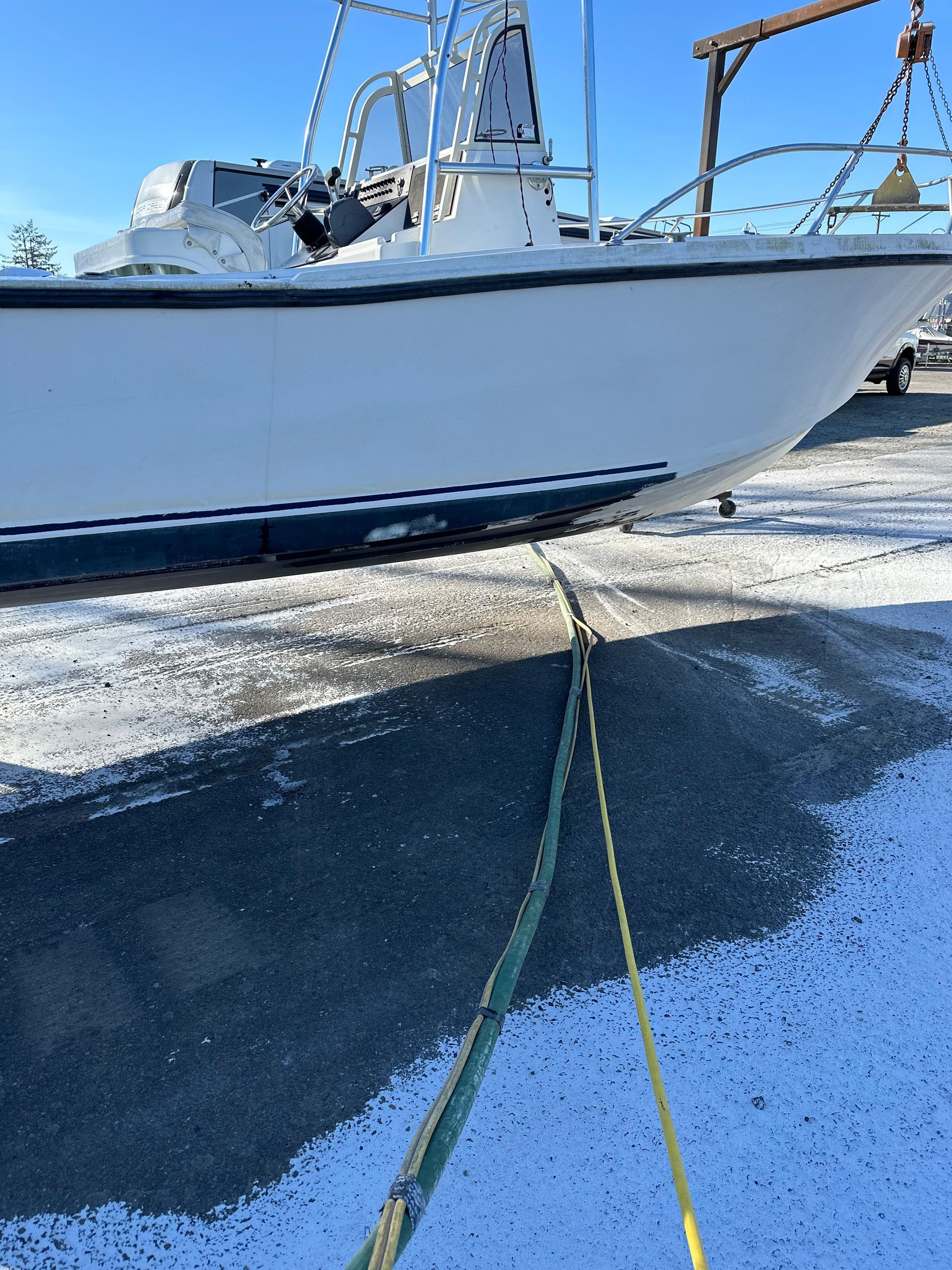 White boat on snowy asphalt, pulled by two yellow ropes.