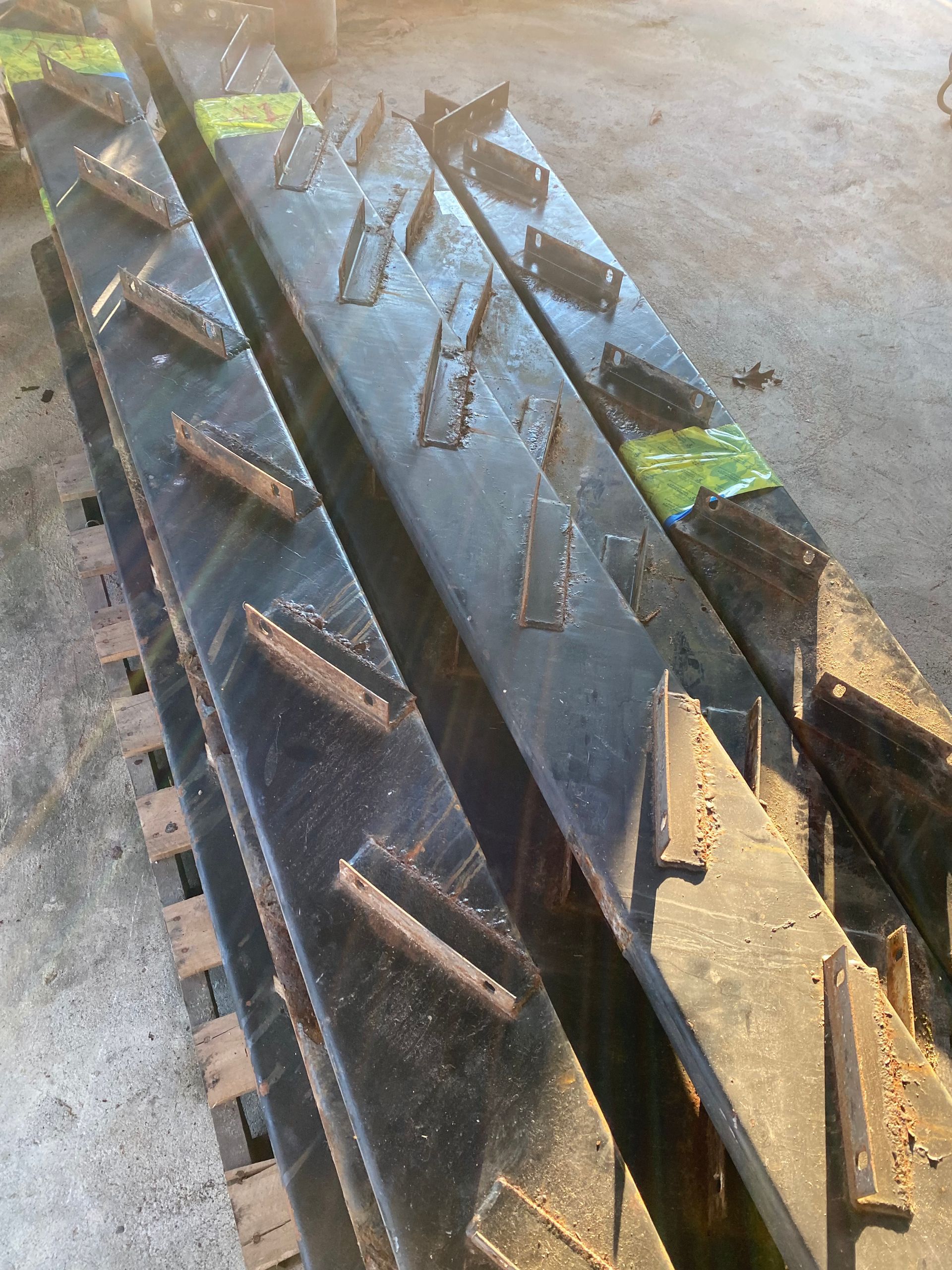 Black metal agricultural equipment with angled blades, stacked on a cement surface.