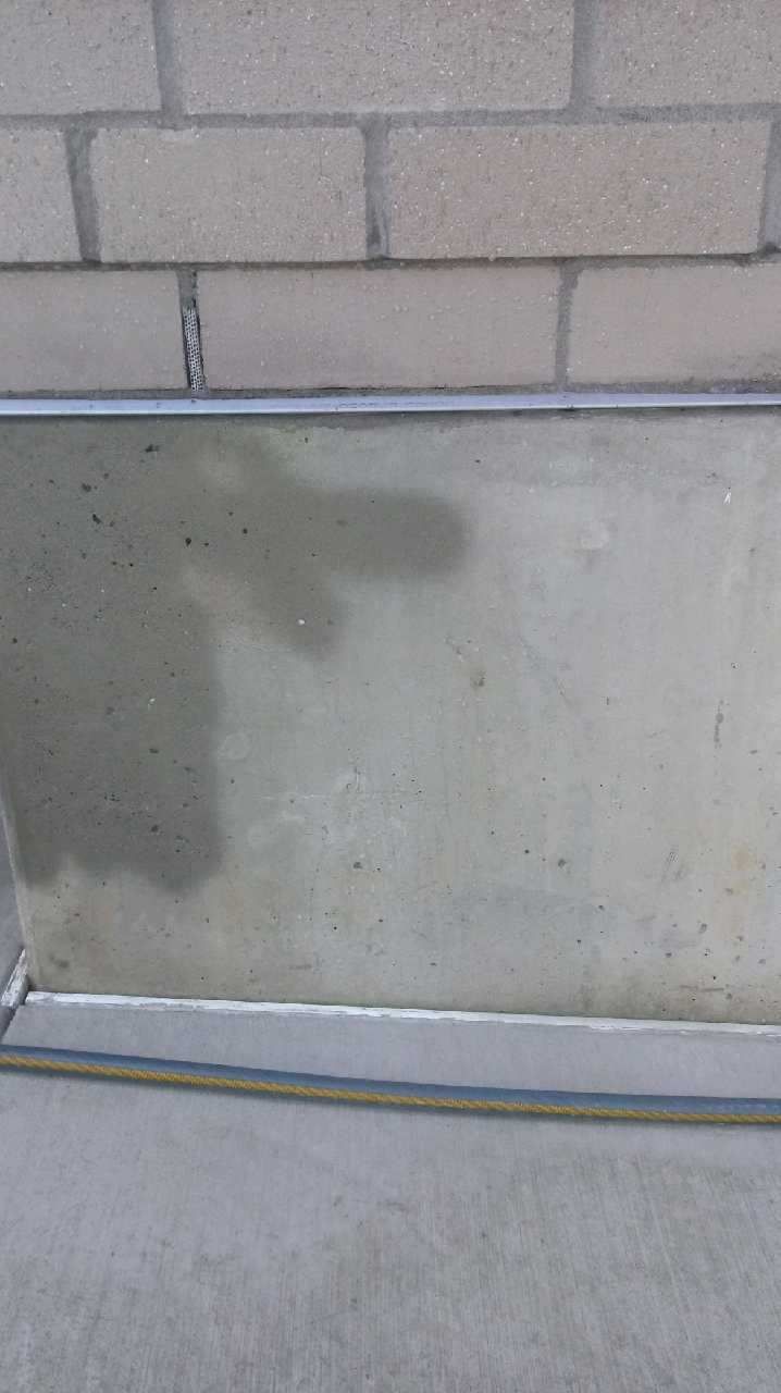 Close-up of a concrete wall with a metal trim and a section of a blue hose. Brick wall is above.