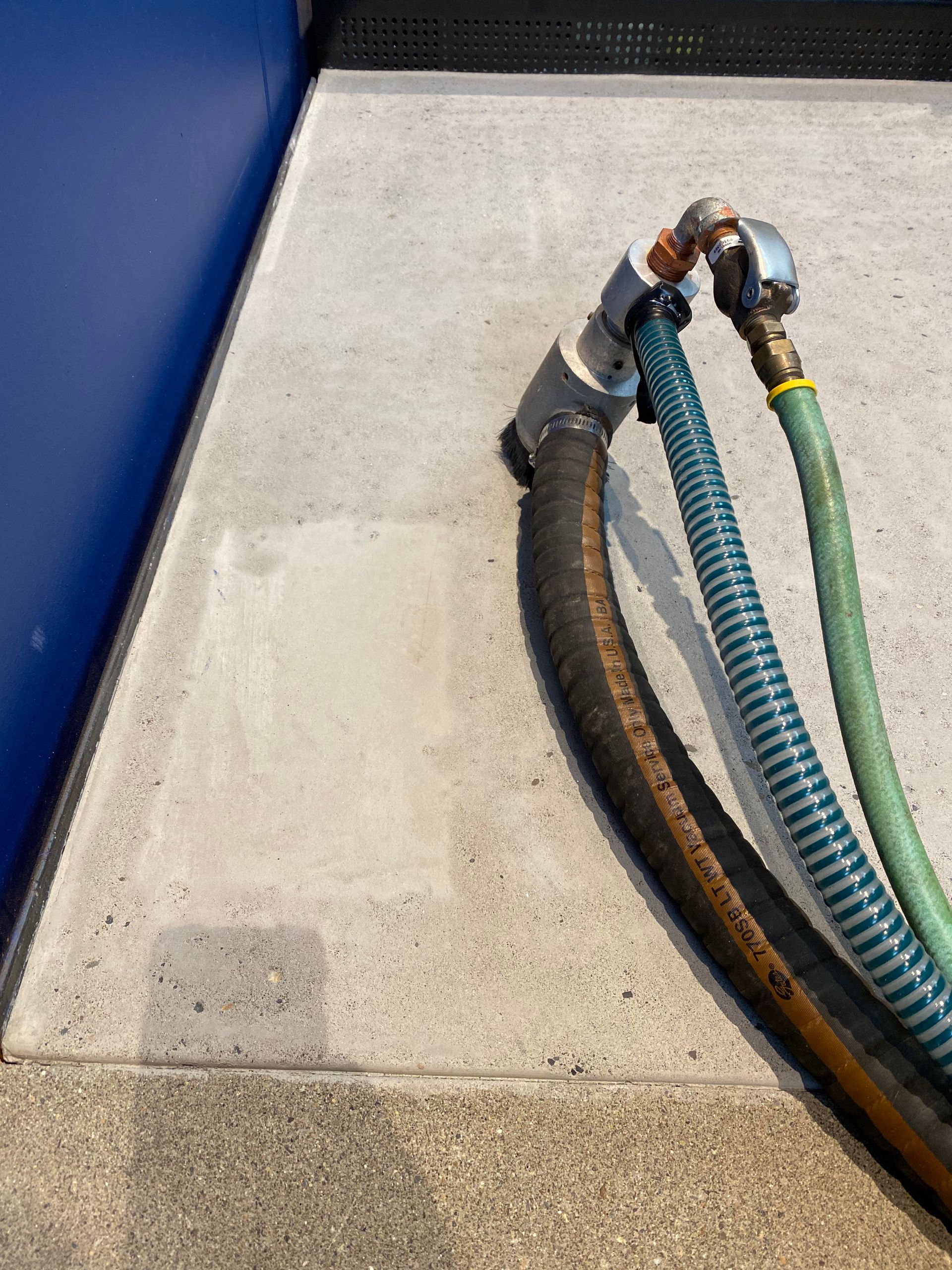 Hoses attached to a metal fixture on a concrete surface, near a blue wall.