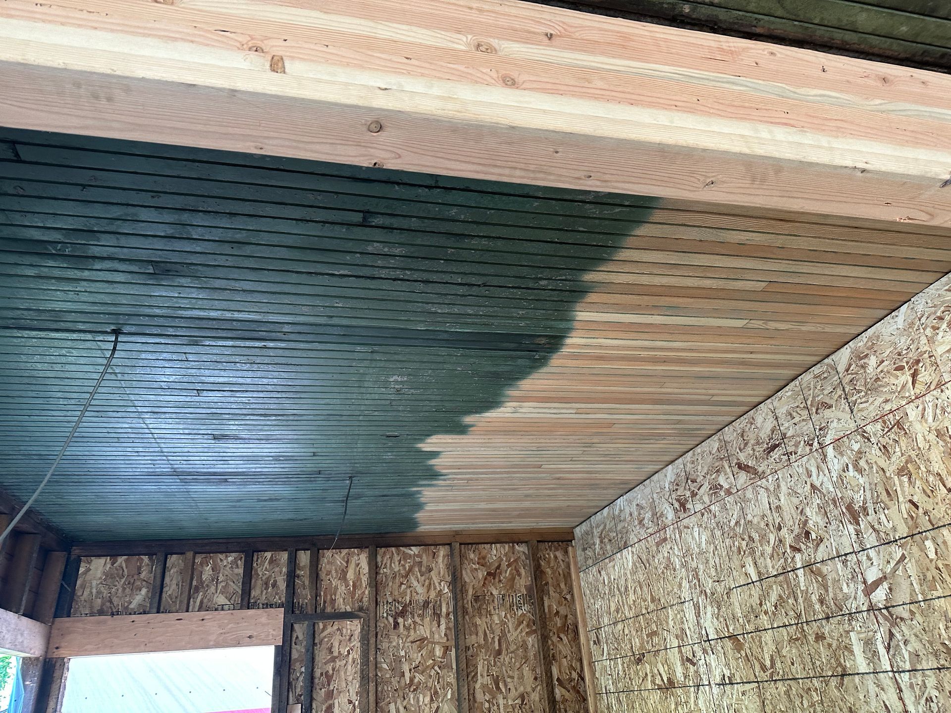 Interior view of a partially constructed building with OSB walls and ceiling covered in green material.
