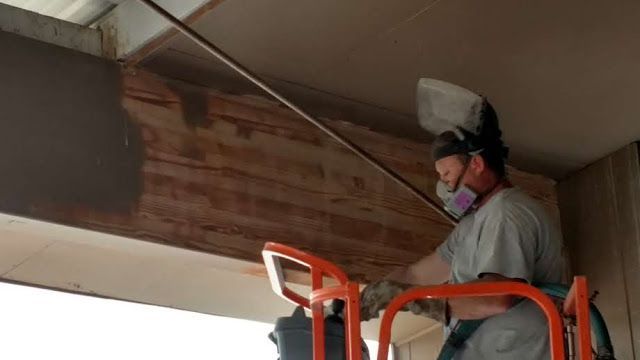 Person wearing protective gear on a lift, welding above a wooden beam.