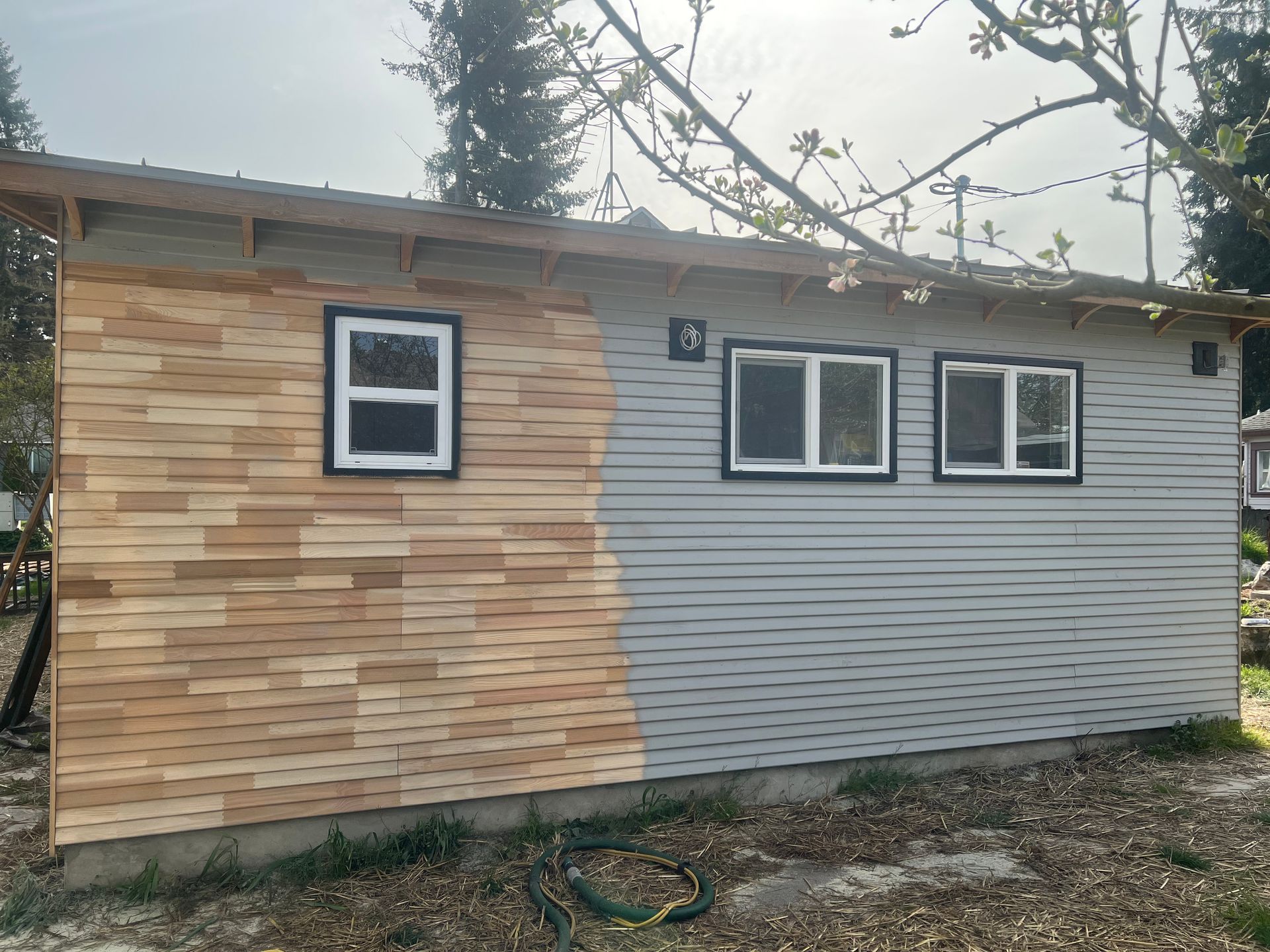Exterior of a building with cedar siding on one side and gray siding on the other, three windows.